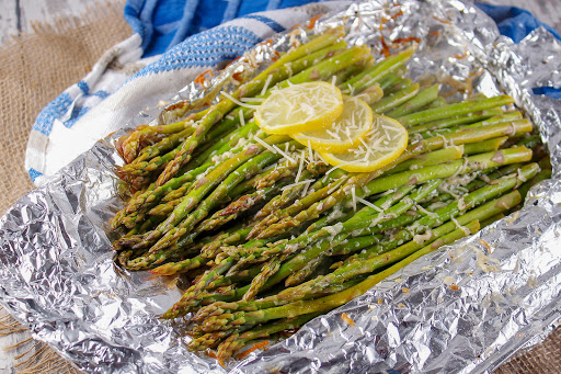BBQ asparagus on aluminum foil with lemon slices.